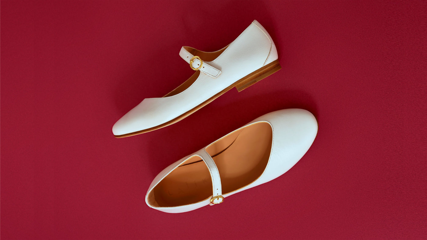 photo of white italian leather, mary jane flats, made in greece, shoes, against a red background